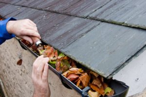 Man de-clogging gutter with lots of leaves