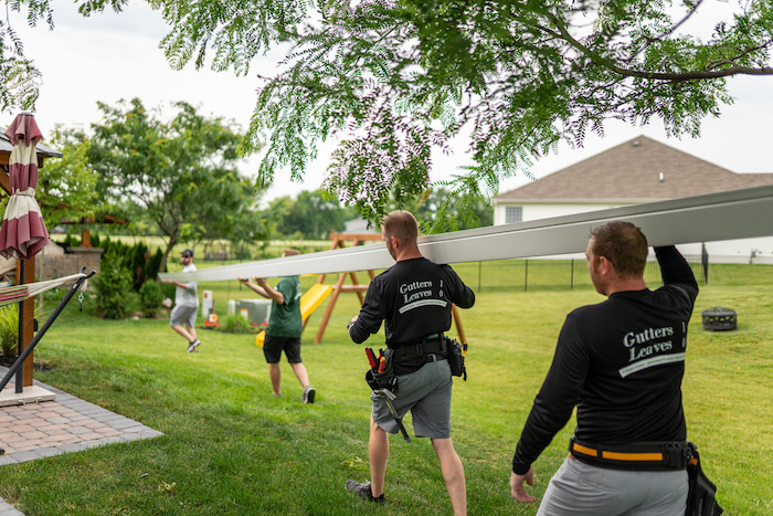 K-Guard team members carrying a gutter across a lawn before installation